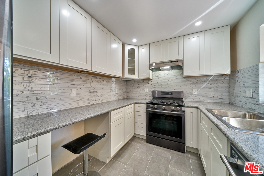 a kitchen with granite countertop stainless steel appliances sink stove and cabinets