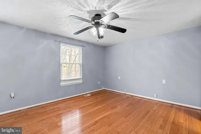 an empty room with wooden floor chandelier fan and windows