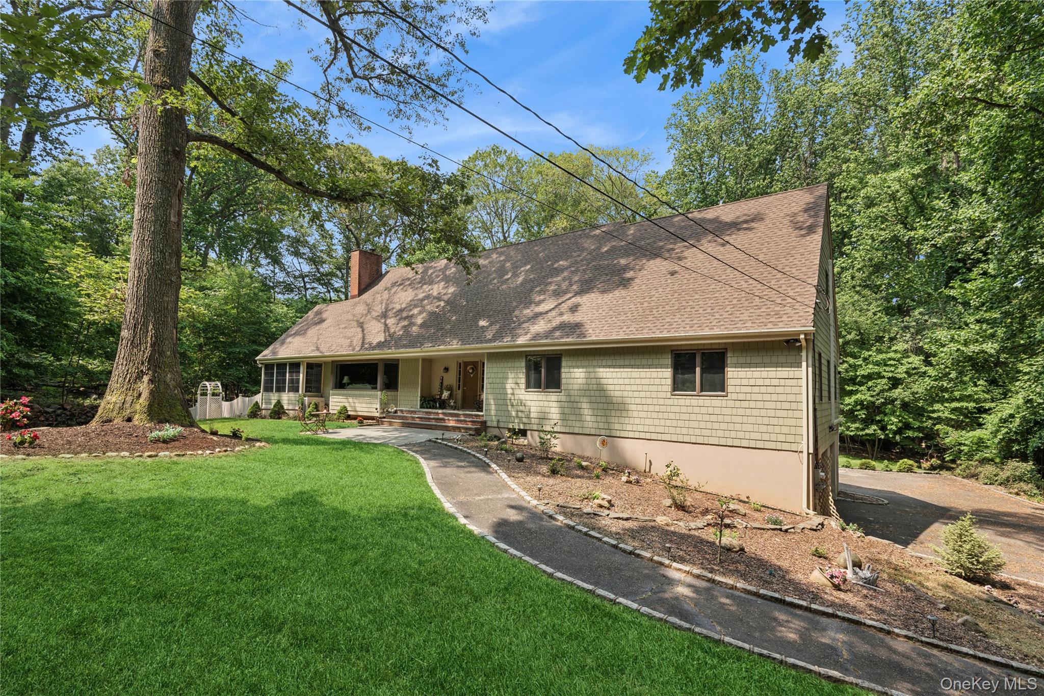View of front of home featuring a chimney, covered porch, a front yard, and a shingled roof