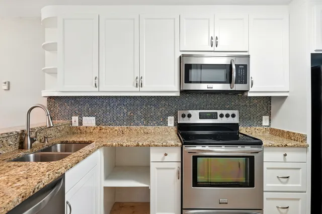 a kitchen with granite countertop white cabinets and stainless steel appliances