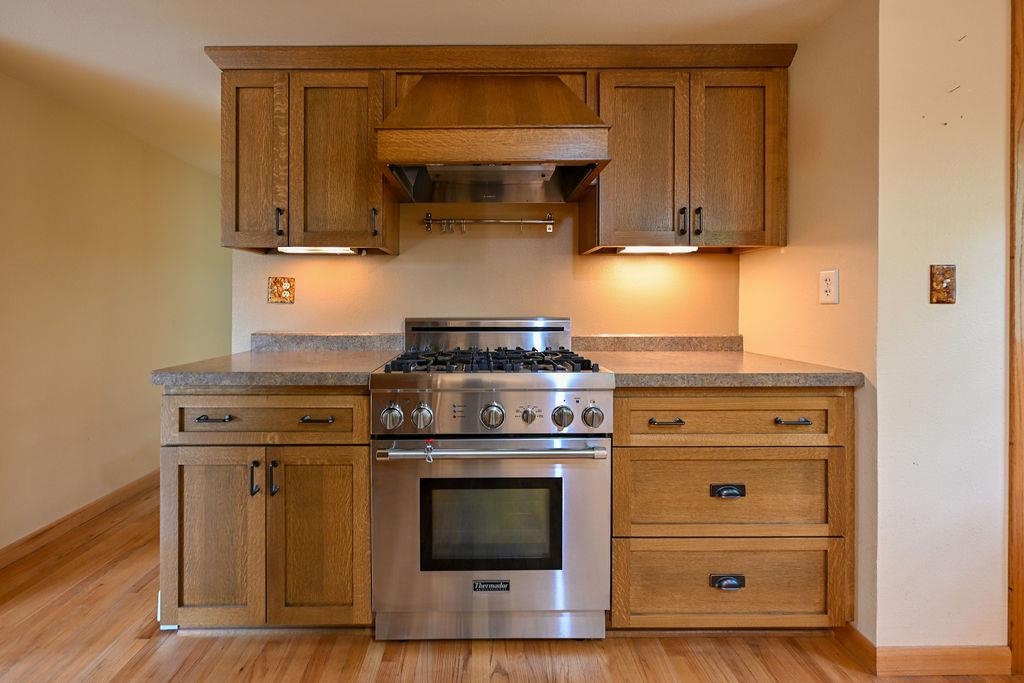 3705 County Rd D Poplar, WI 54864 - Photo 6 of 20 Kitchen with high end stainless steel range oven, custom exhaust hood, brown cabinets, and light wood-style floors