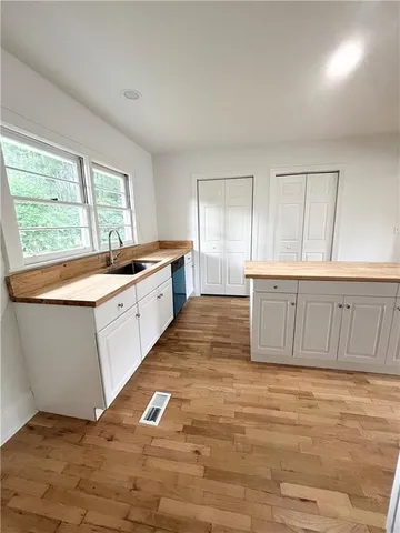 a large kitchen with granite countertop a stove a sink and white cabinets with wooden floor