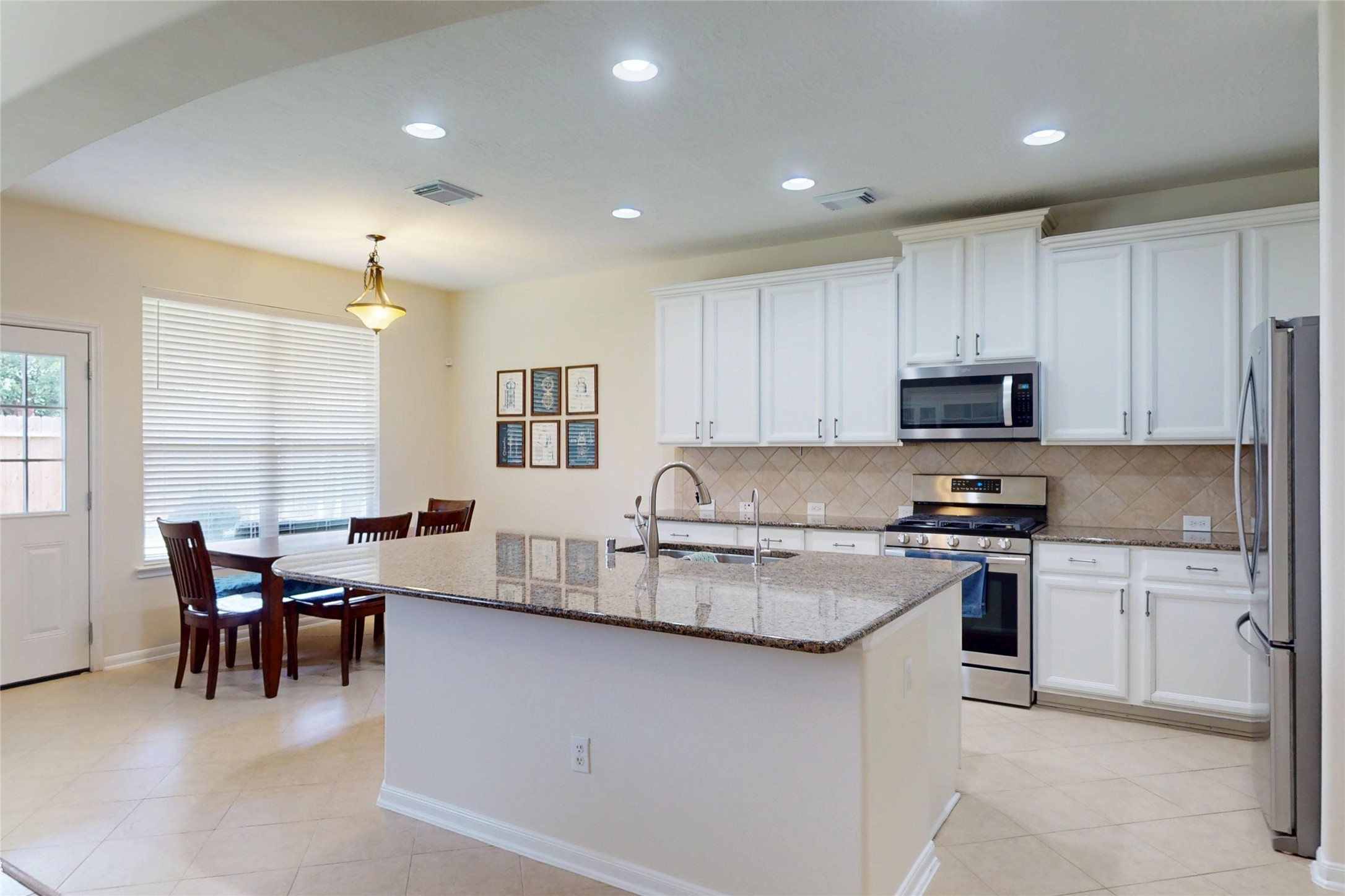 17402 Rainer Valley Lane Humble, TX 77346 - Photo 11 of 33 This bright kitchen features modern stainless steel appliances, white cabinetry, and a large granite island with a built-in sink. Adjacent is a cozy breakfast area with a table, chairs, and ample natural light from a large window.