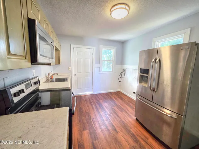 a kitchen with stainless steel appliances granite countertop a refrigerator a stove and a sink with wooden floors