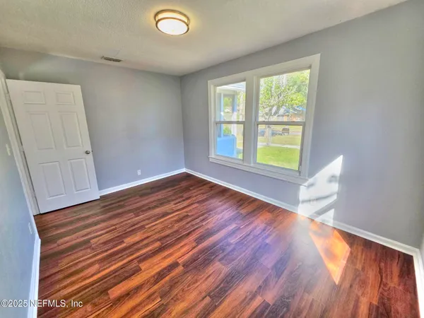 a view of an empty room with wooden floor and a window