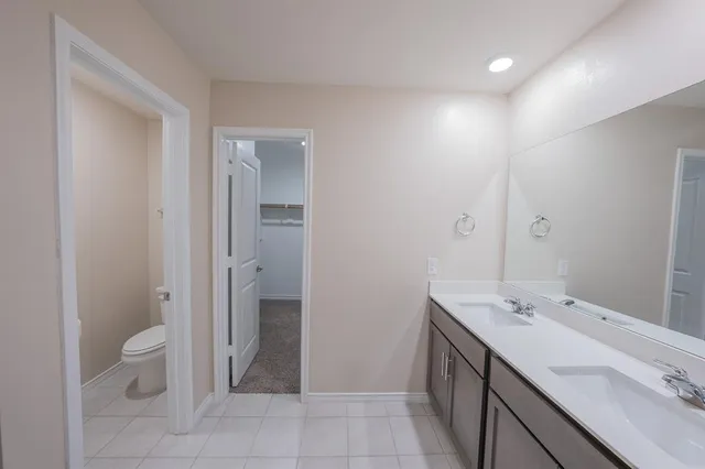 a spacious bathroom with a double vanity sink a toilet and a mirror