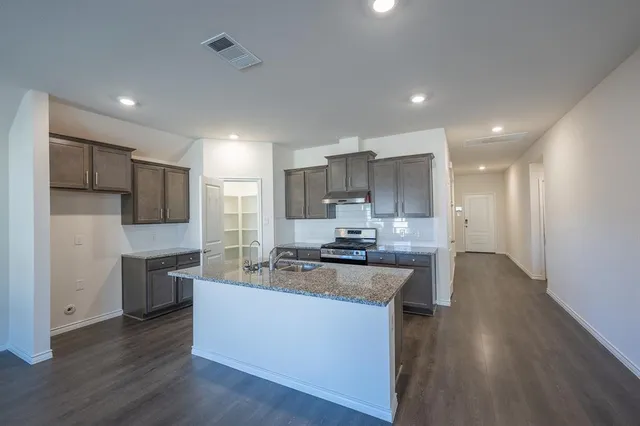 a large kitchen with stainless steel appliances kitchen island granite countertop a stove a sink a refrigerator and white cabinets with wooden floor