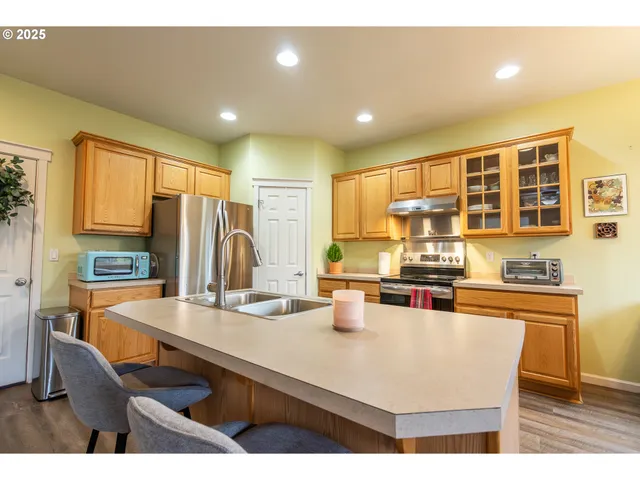 a kitchen with stainless steel appliances granite countertop a stove a sink a refrigerator white cabinets and wooden floor