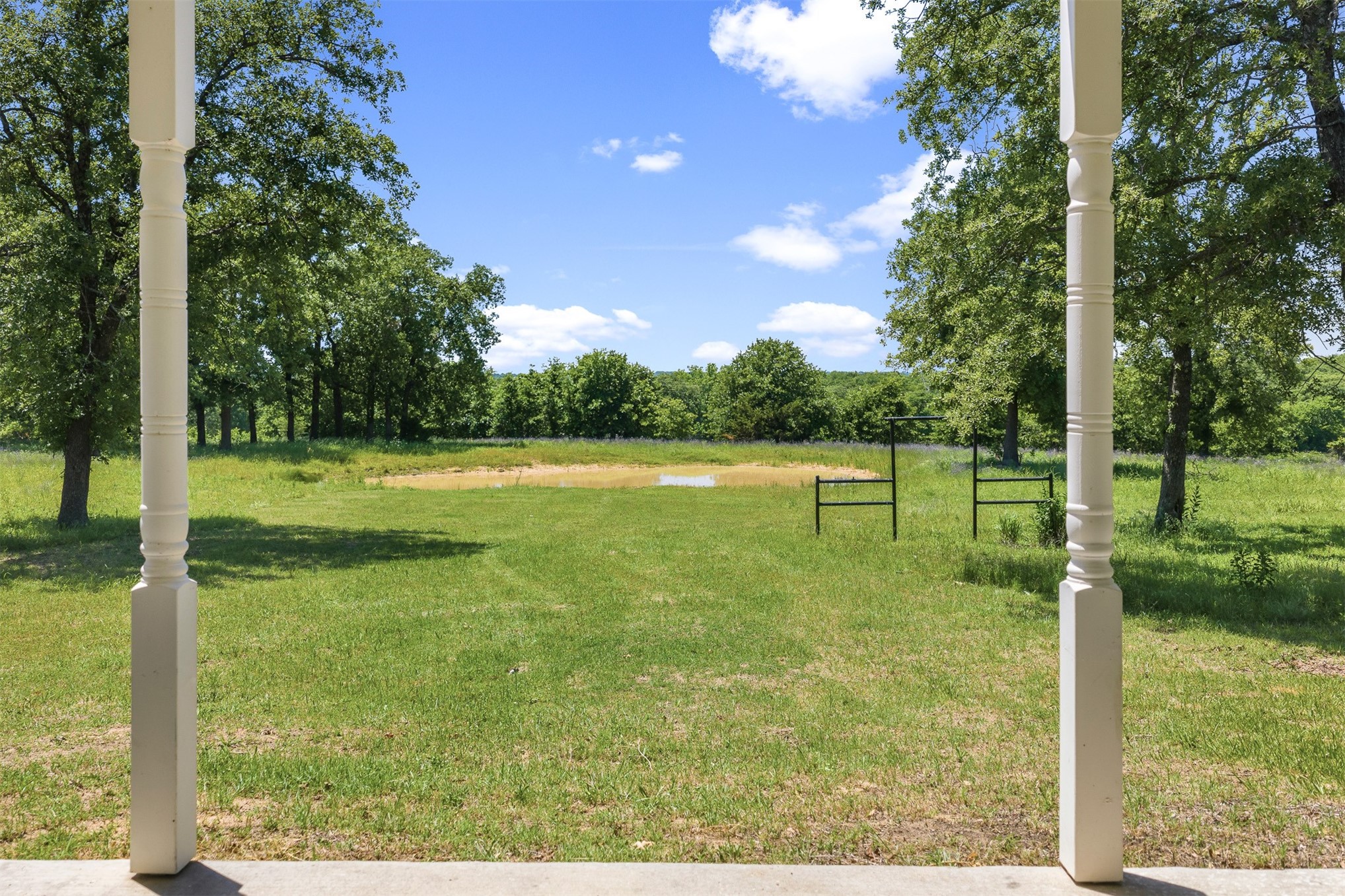 831 Barrons Ridge Wilson, OK 73463 - Photo 32 of 47 Expansive green lawn framed by mature trees, featuring a prominent pond and distant woodlands under a clear sky