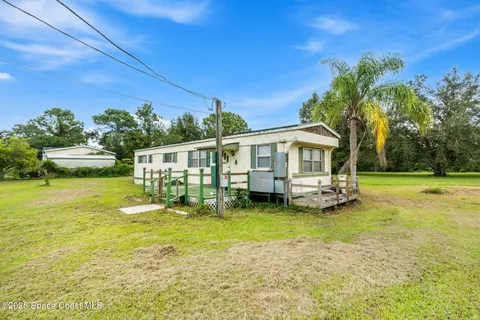 a view of a white house with a big yard and potted plants