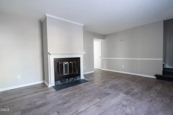 a view of an empty room with wooden floor fireplace and a window