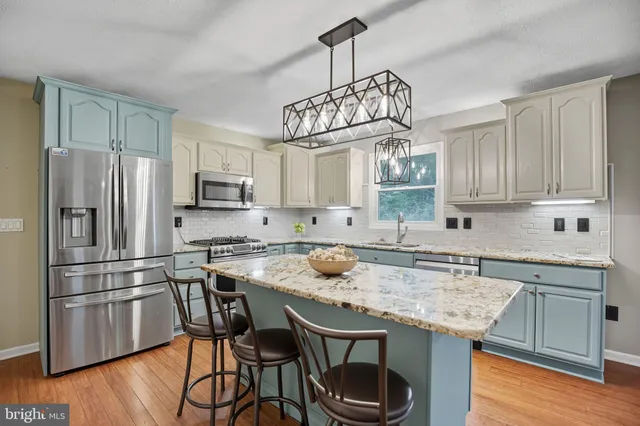 a kitchen with stainless steel appliances granite countertop a sink a stove a refrigerator and island with wooden floor