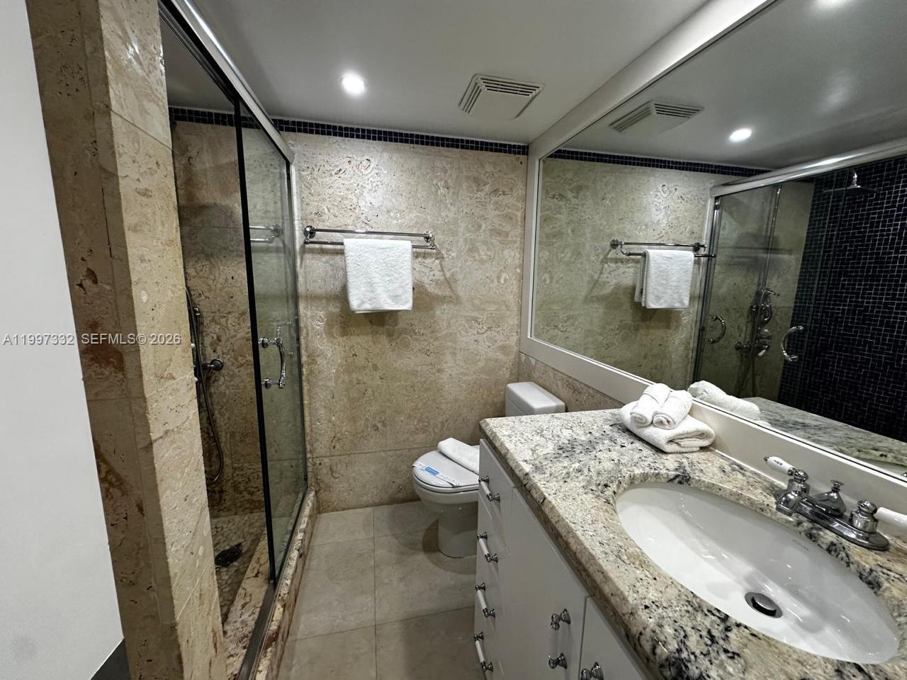 5225 Collins Avenue, Unit 614 Miami Beach, FL 33140 - Photo 2 of 8 a bathroom with a granite countertop sink a toilet and shower