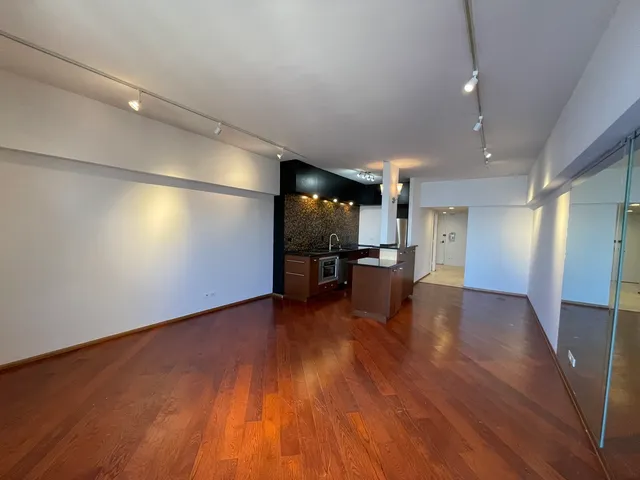 an empty room with wooden floor and a kitchen