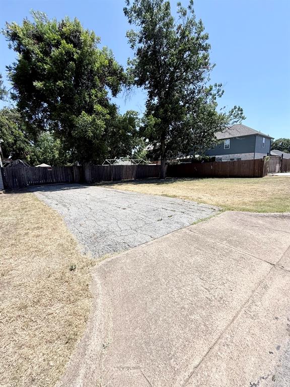 Expansive lot featuring mature trees, a wooden fence, and concrete paving