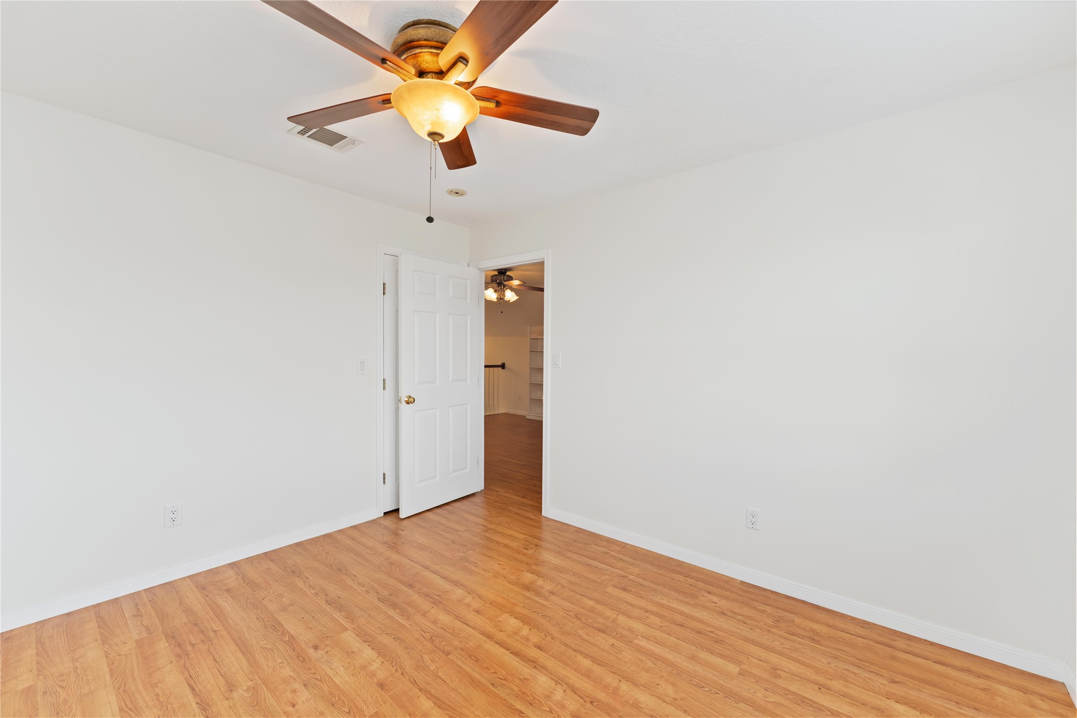 606 Packer Court Webster, TX 77598 - Photo 6 of 28 This room features a ceiling fan with light, wood flooring, and freshly painted white walls. It has a door leading to another space, creating an open, airy feel.