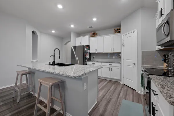 a kitchen with stainless steel appliances kitchen island granite countertop a stove top oven a sink a dining table and chairs with wooden floor