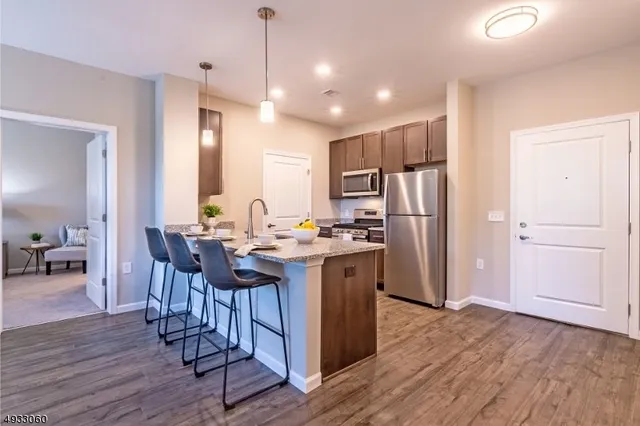 a kitchen with stainless steel appliances granite countertop a refrigerator a stove a sink dishwasher and a dining table with wooden floor