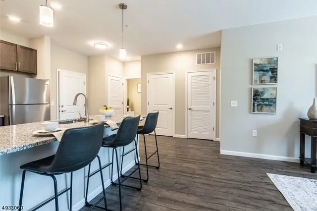 a dining hall with stainless steel appliances kitchen island granite countertop a dining table chairs and a refrigerator