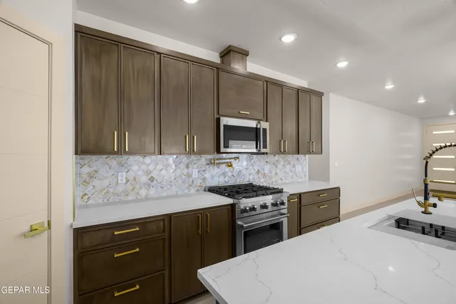 a large kitchen with stainless steel appliances a large counter top a stove a sink dishwasher and a refrigerator