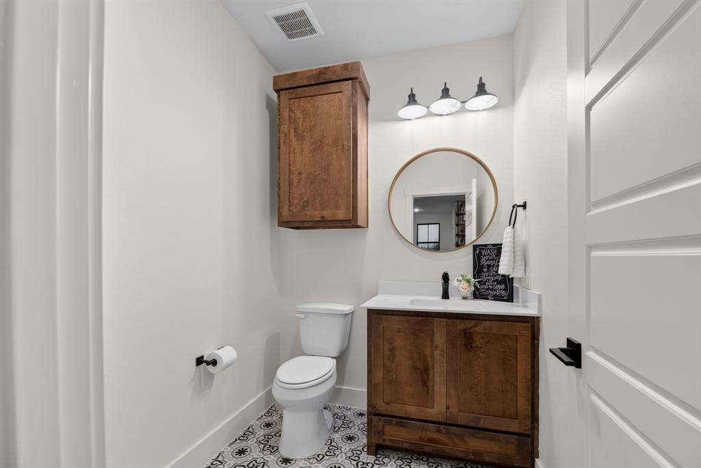 985 Vest Lane Pilot Point, TX 76258 - Photo 25 of 40 Modern vanity with white countertop, round mirror, and patterned floor tile