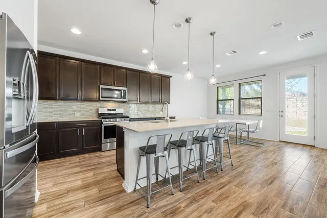 a kitchen with stainless steel appliances granite countertop a stove top oven a sink dishwasher a dining table and chairs with wooden floor