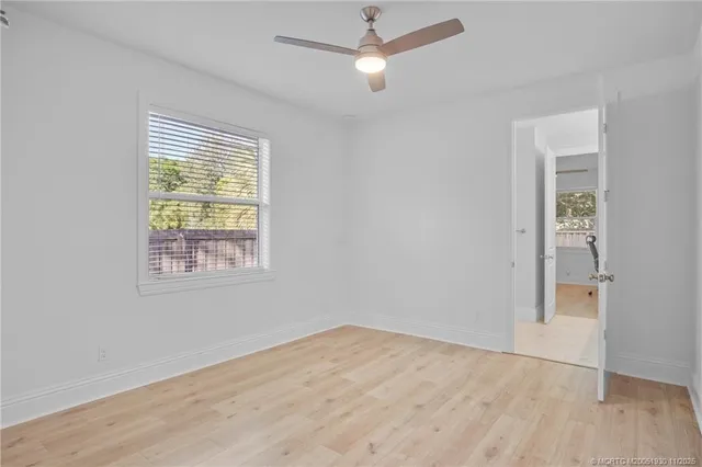 an empty room with wooden floor ceiling fan and windows