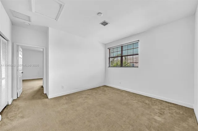 an empty room with windows and view of kitchen