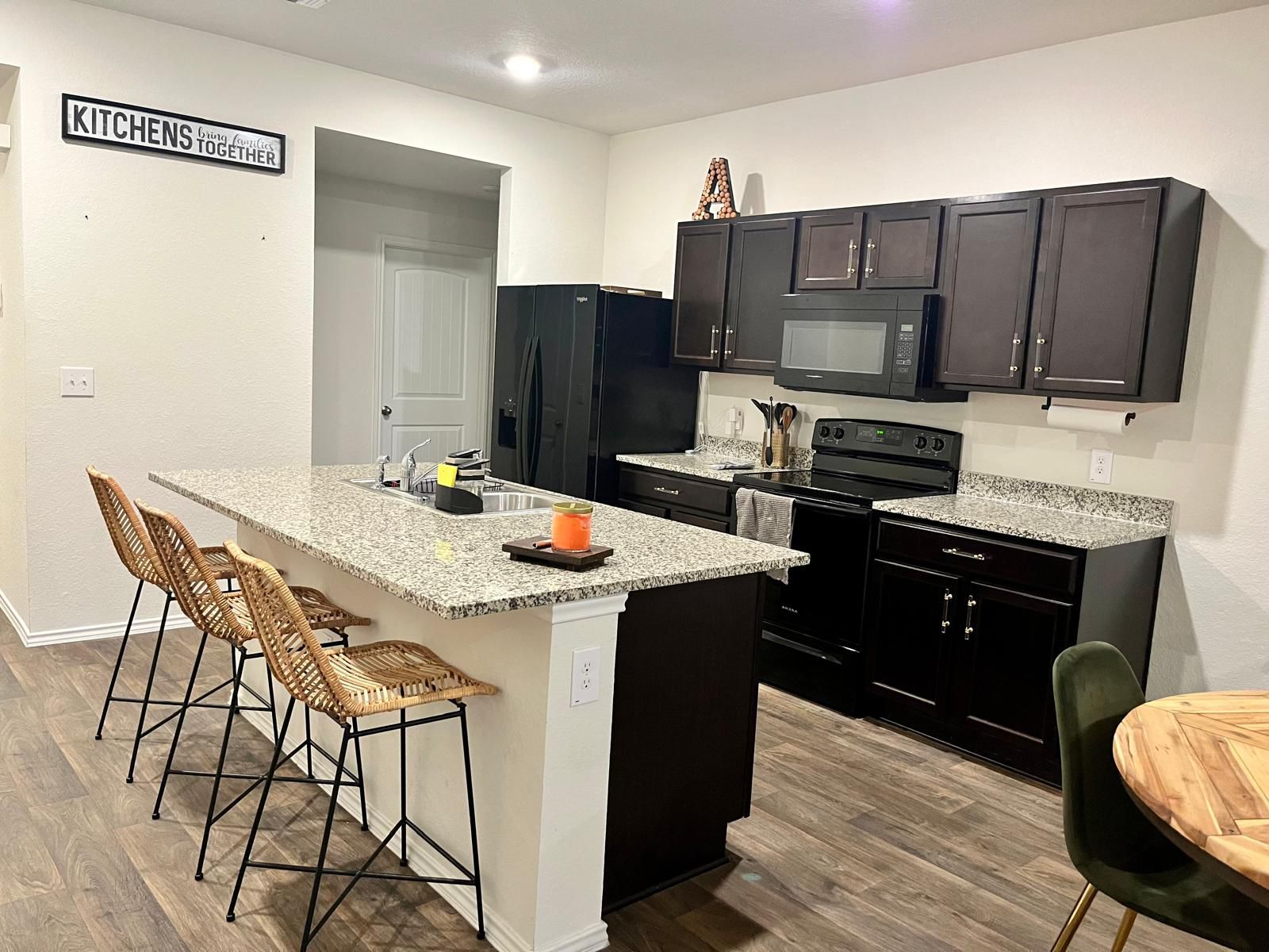 15006 Breccia Road Manor, TX 78653 - Photo 2 of 8 a kitchen with stainless steel appliances kitchen island granite countertop a sink dishwasher a stove a refrigerator with a dining table and chairs
