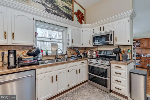 a kitchen with stainless steel appliances granite countertop a sink dishwasher stove and white cabinets