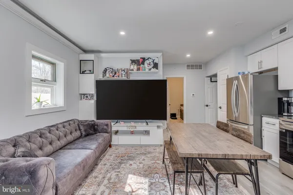 a living room with stainless steel appliances furniture a flat screen tv and a window