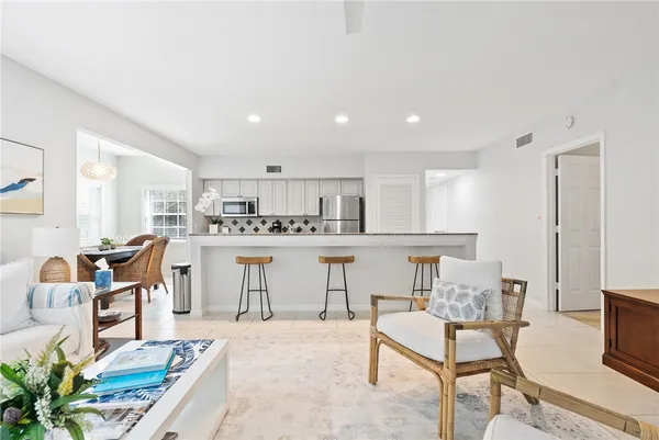 a room with stainless steel appliances kitchen island granite countertop a dining table chairs and a refrigerator