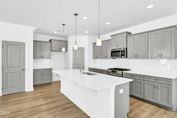 a large kitchen with stainless steel appliances a stove a sink a refrigerator and white cabinets with wooden floor