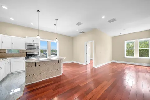 a kitchen with granite countertop a stove a sink and white cabinets with wooden floor next to windows