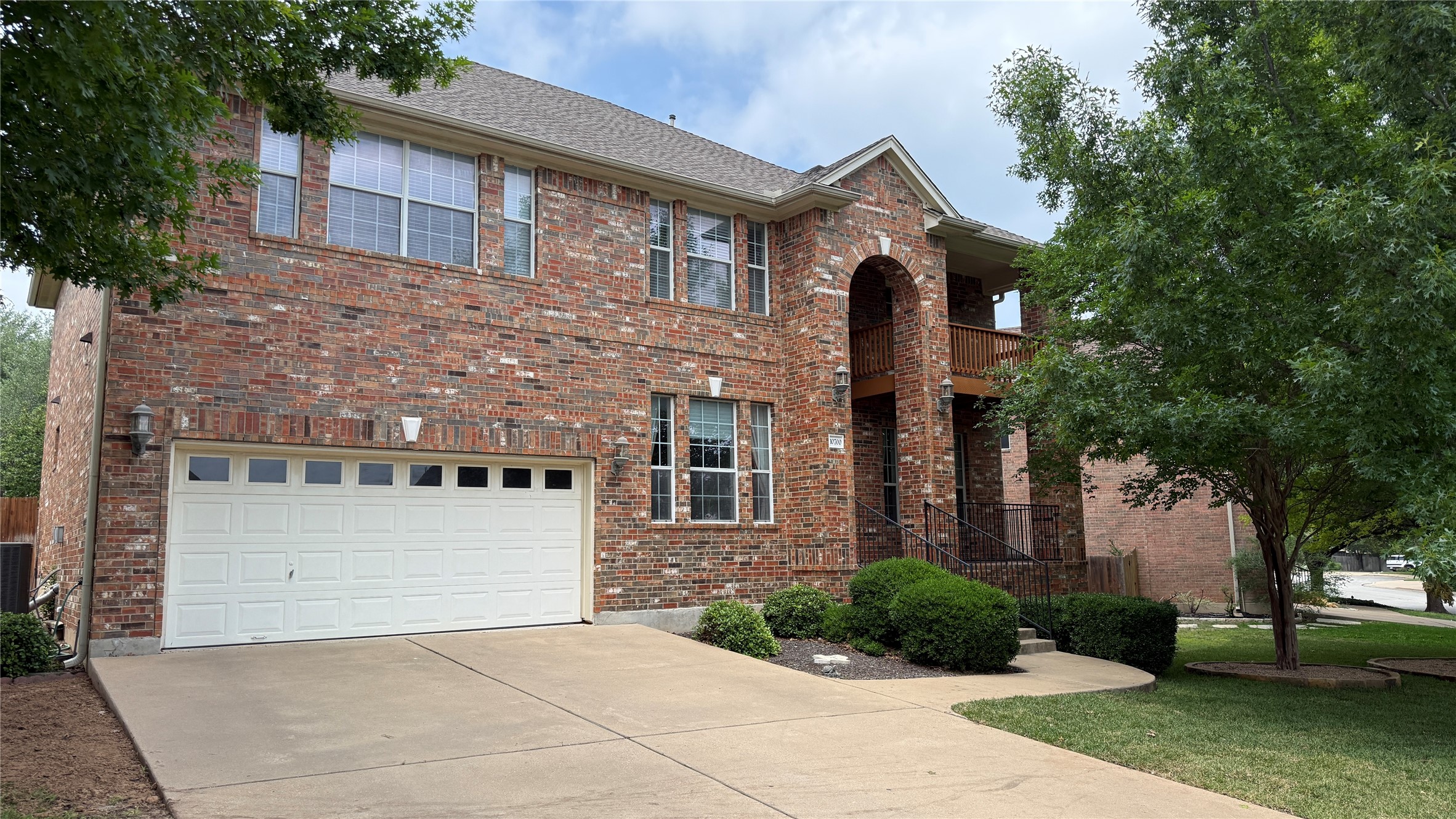 10700 Pointe View Drive Austin, TX 78738 - Photo 2 of 22 Brick exterior residence featuring a two-car garage, concrete driveway, arched entryway, and upper-level balcony with wood railing