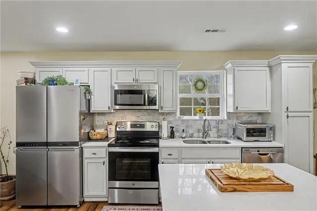 a kitchen with stainless steel appliances a stove a refrigerator a sink and white cabinets
