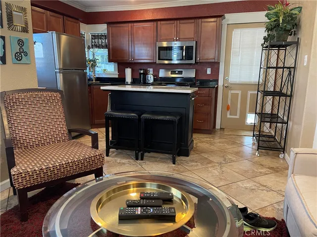 a living room with stainless steel appliances furniture a rug and a kitchen view