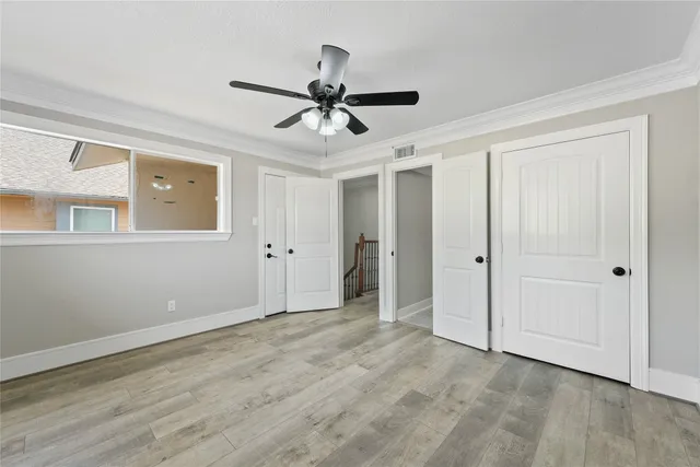 a view of an empty room with wooden floor and a ceiling fan