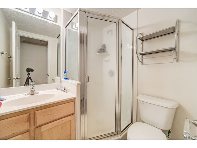 865 North 500 West, Unit 5 Provo, UT 84604 - Photo 6 of 14 Bathroom featuring a glass-enclosed shower, a vanity with wood cabinetry and a white countertop, a mirror with strip lighting, and a white toilet