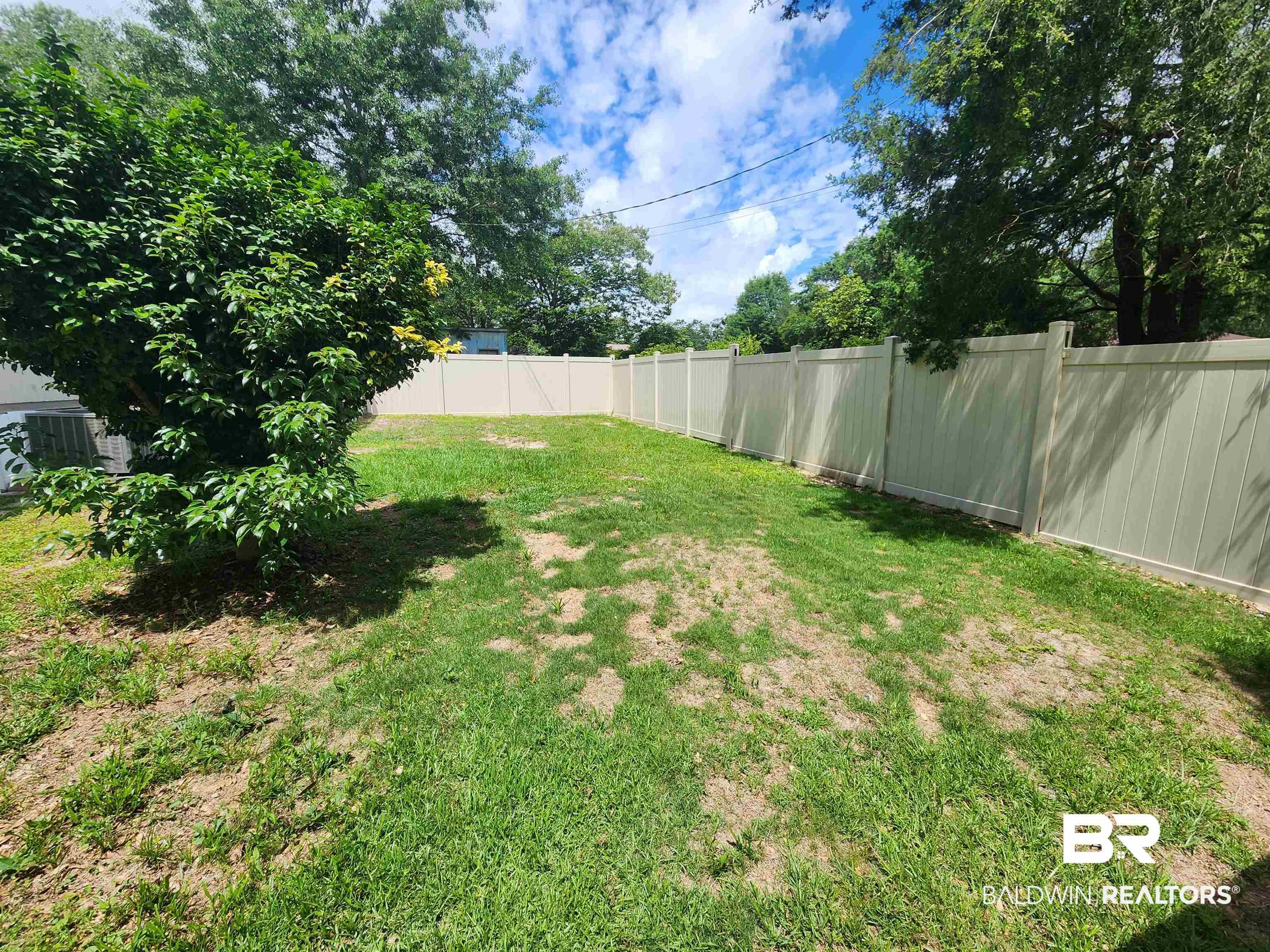 23051 Fritz Lane Foley, AL 36535 - Photo 4 of 26 Expansive grass lawn featuring a complete perimeter privacy fence, mature trees, and established shrubbery