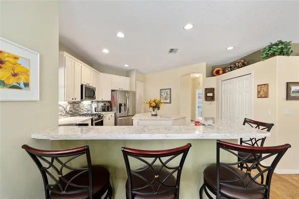 a kitchen with stainless steel appliances kitchen island granite countertop a dining table chairs and a refrigerator