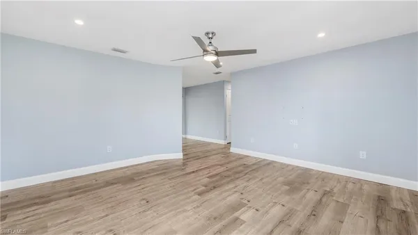 an empty room with wooden floor ceiling fan and windows