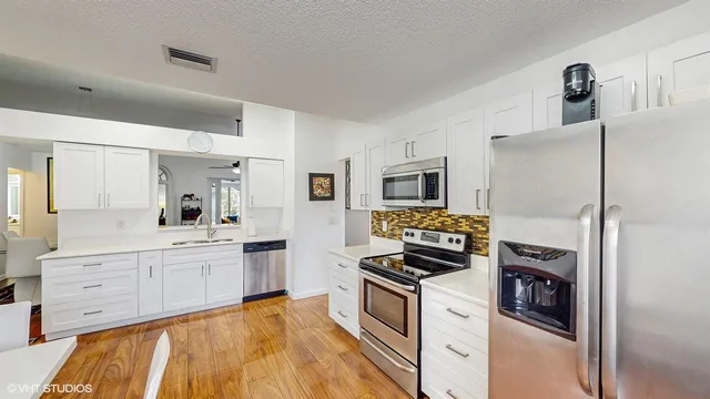 a kitchen with stainless steel appliances a refrigerator a stove a sink and white cabinets