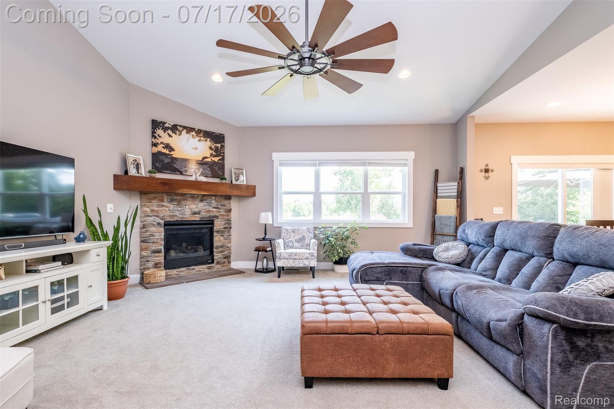 12349 Sugar Maple Drive Fenton, MI 48430 - Photo 8 of 67 Spacious living area featuring a vaulted ceiling with a large ceiling fan, a stone-faced fireplace with a wood mantel, light-toned carpeting, and multiple windows for natural light