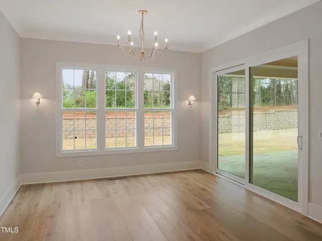 an empty room with wooden floor chandelier and windows