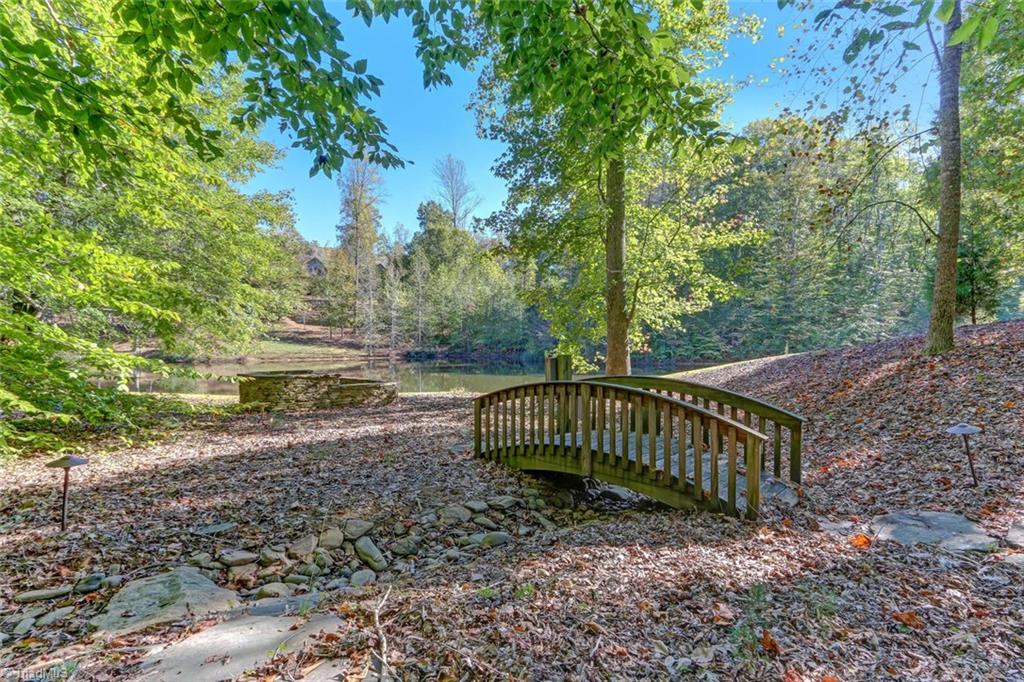 5260 Bunch Road Summerfield, NC 27358 - Photo 26 of 30 Shown here is a bridge over a stream bed which, when operational, recirculates water from the pond to the stream head and back to the pond. Raised fire pit in the background with the pond beyond.