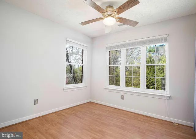 an empty room with wooden floor fan and windows
