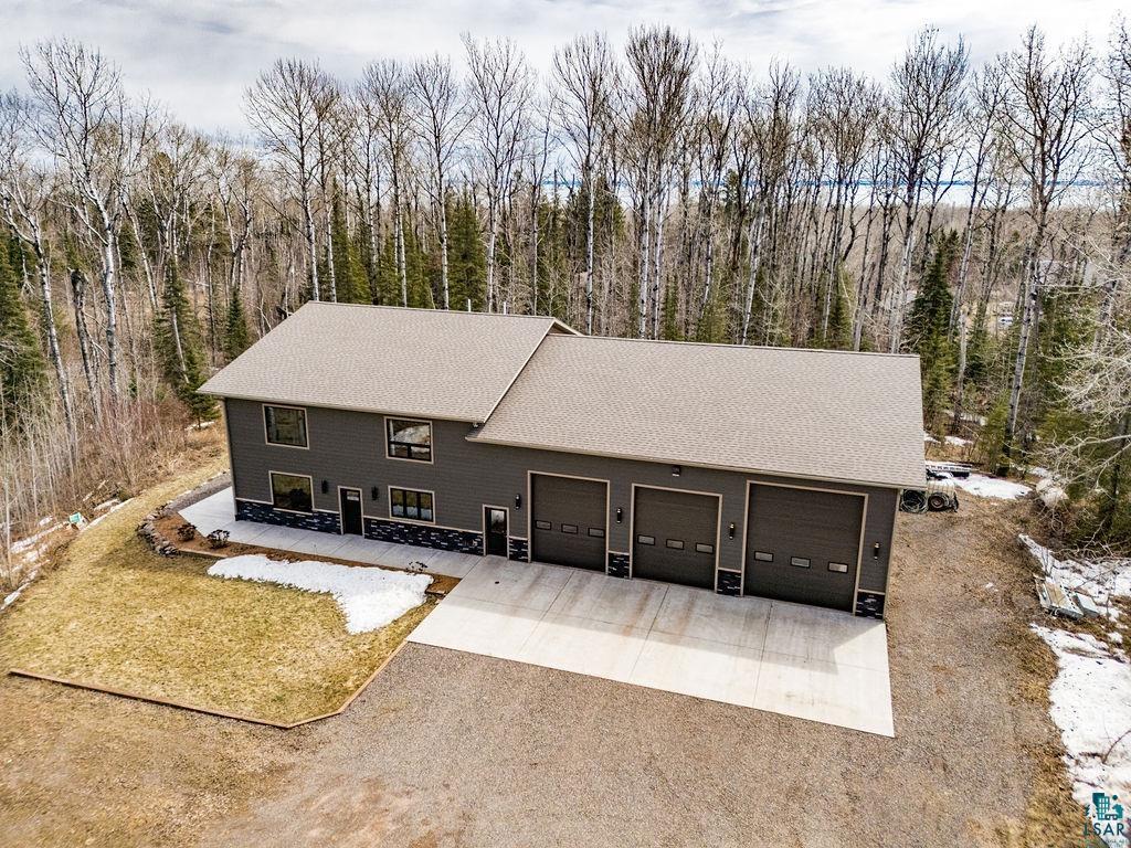 View of front of home with driveway, a shingled roof, a garage, and a forest view