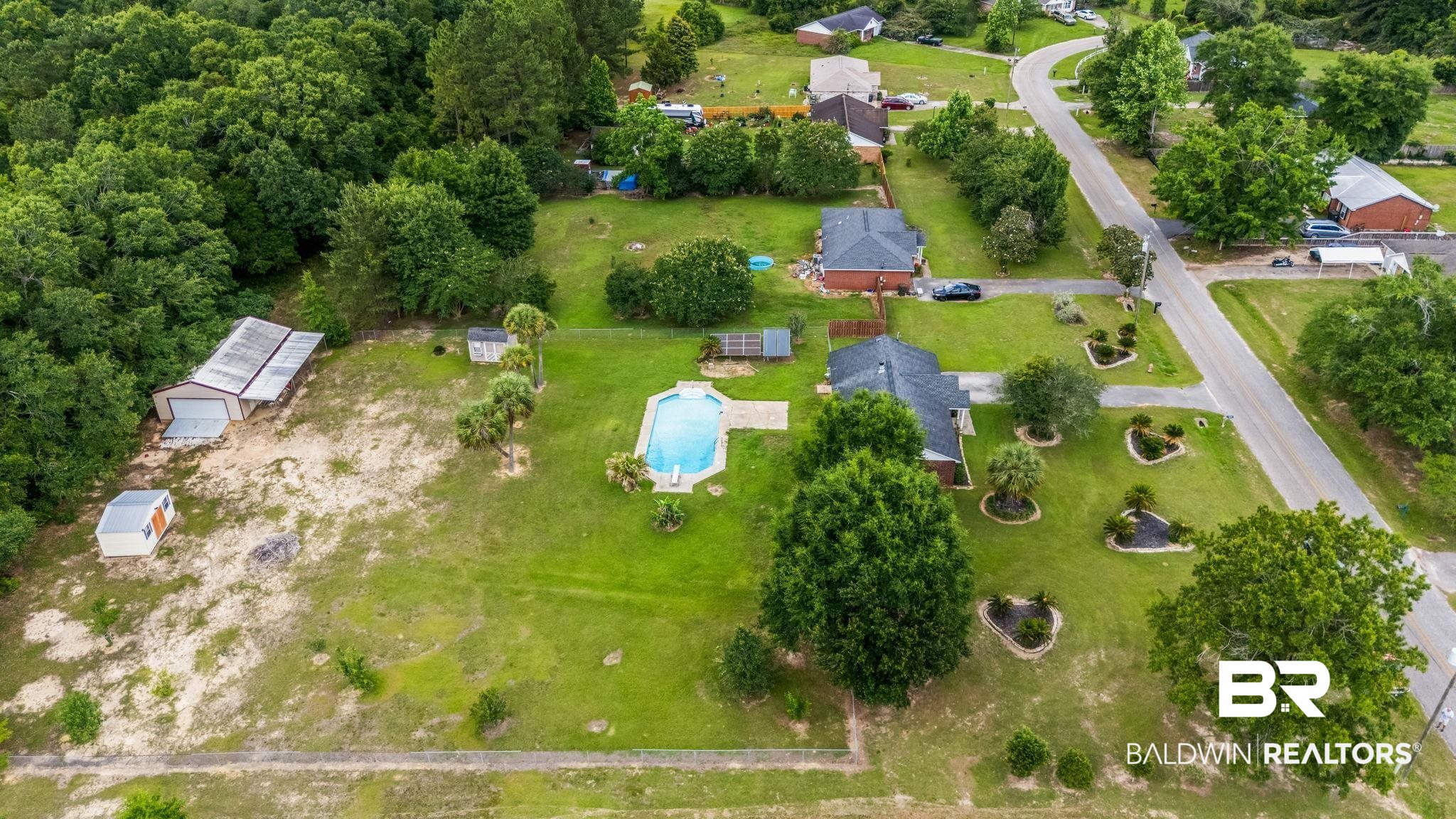 15096 Highland Circle Foley, AL 36535 - Photo 43 of 52 Expansive property featuring a large in-ground swimming pool with surrounding patio, a primary residence with a dark shingle roof, a separate multi-bay metal outbuilding, and a secondary small outbuilding