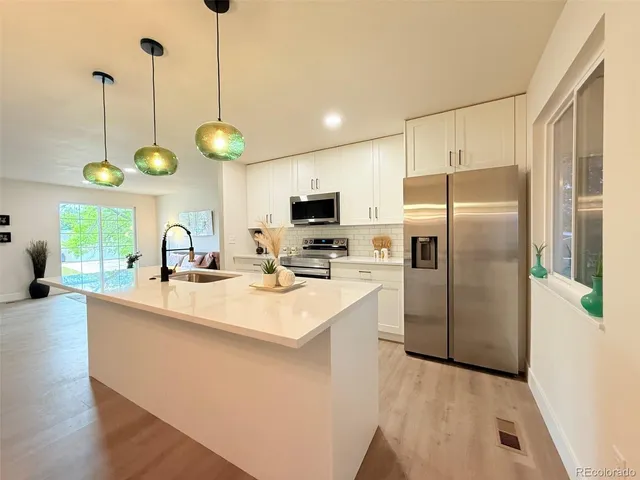 a kitchen with stainless steel appliances a stove a sink a refrigerator a center island with wooden floor and cabinets